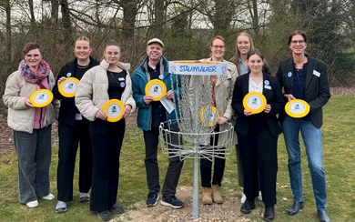 Gruppe von acht Personen mit Discgolf-Scheiben vor einem Discgolf-Korb