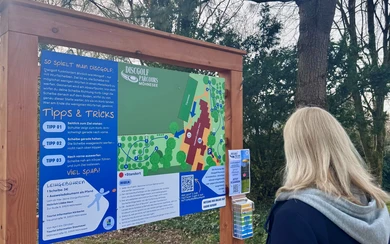 Infotafel.jpg Person liest Informationstafel mit Tipps & Tricks am Discgolf-Parcours Möhnesee