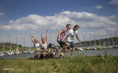 Gruppe junger Menschen zieht fröhlich einen Bollerwagen am Möhneseeufer entlang
