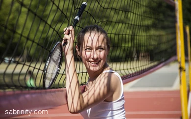 Person hält einen Federballschläger am Netz auf einem Tennisplatz.