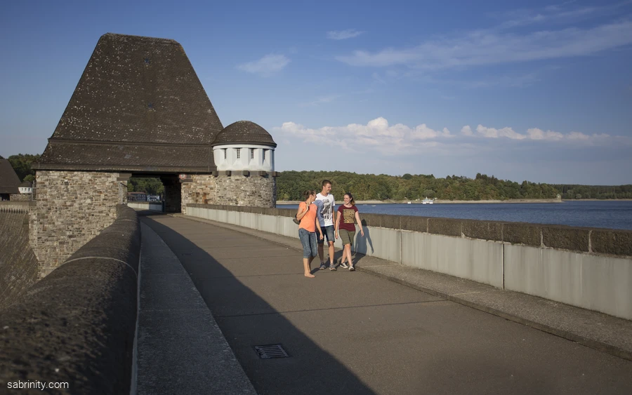 Drei Personen spazieren über die Staumauer mit Blick auf den Möhnesee.