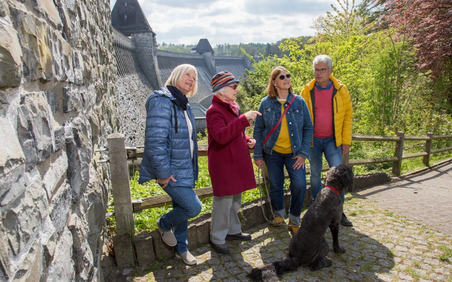 Kleingruppe am Plateau der Staumauer Gruppe von Personen mit Hund steht etwas unterhalb an der Staumauer.