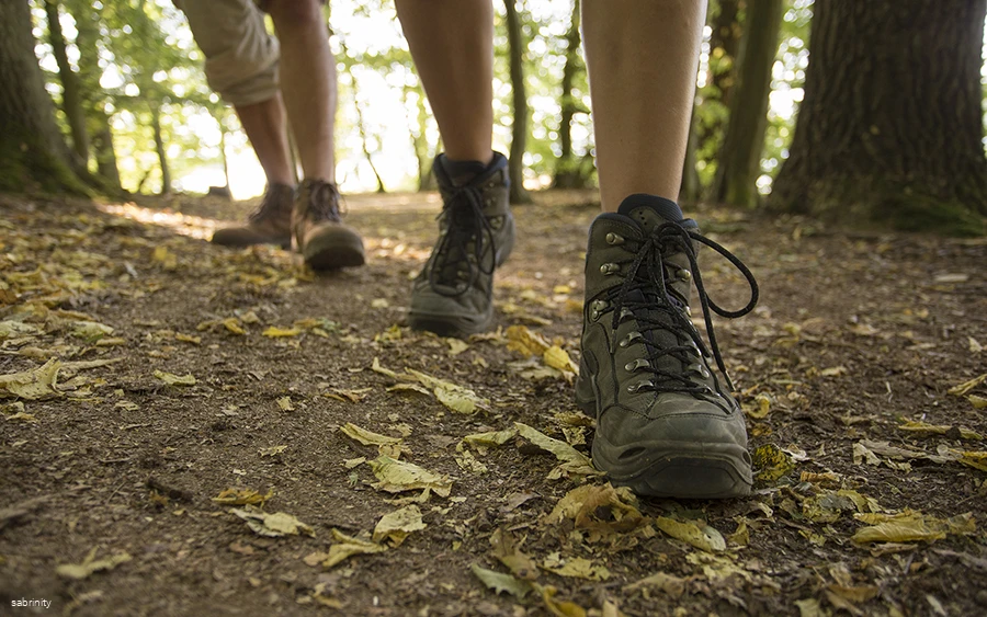 Nahaufnahme von den Beinen zweier Personen in Wanderschuhen auf einem Waldweg.