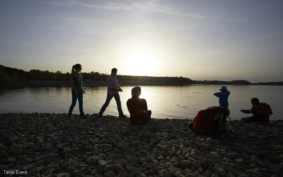 Silhouetten von Personen an einem Seeufer bei Sonnenuntergang.