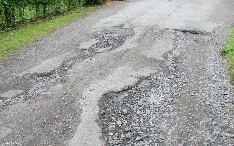 Straße mit großen Schlaglöchern und beschädigtem Asphalt