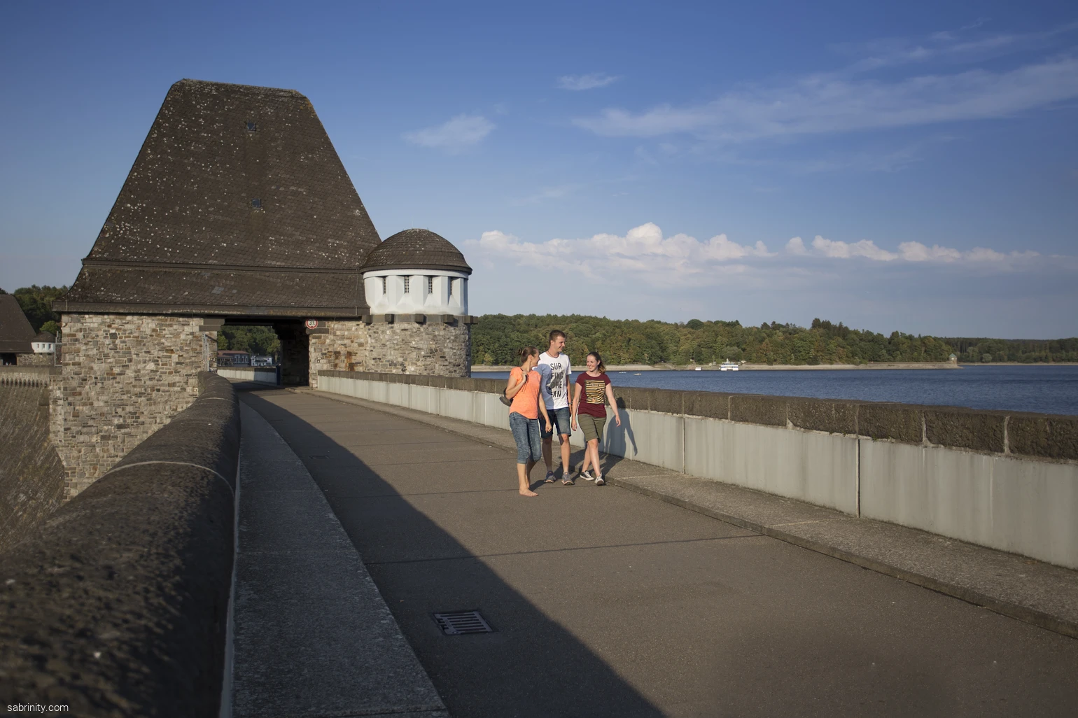 Drei Personen spazieren über die Staumauer mit Blick auf den Möhnesee.